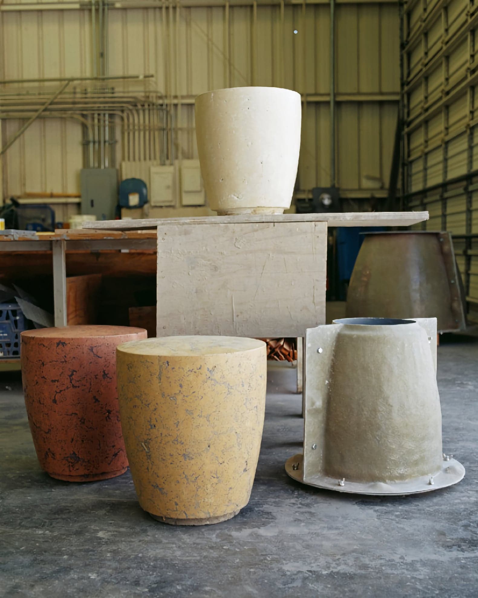 Mottled terracotta and yellow cylindrical stools beside their fiberglass casting molds on the workshop floor
